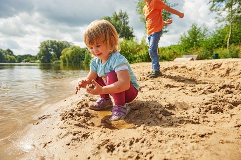 Ein kleines Mädchen spielt im Sand am Vörder See, dahinter ist ein Junge zu sehen