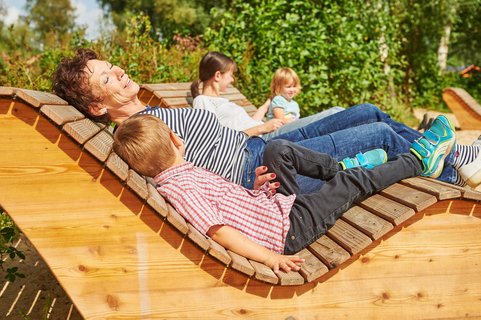 Eine Familie mit Oma und Enkel im Vordergrund genießt die Sonne auf geschwungenen Holzliegen