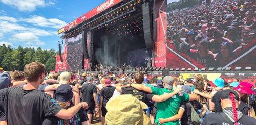 Ein begeistertes Festivalpublikum umarmt sich vor einem großen Bühnenbildschirm mit Live-Performance.