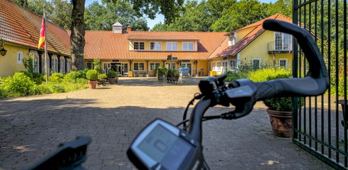 Im Vordergrund ist das Lenkrad eines Fahrrads zu sehen, während im Hintergrund das gelbe Gebäude vom LandPark Lauenbrück sichtbar ist.