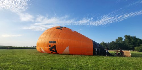 Der halb gefüllte Heißluftballon liegt mit dem Korb auf der grünen Wiese, der Himmel strahlt blau