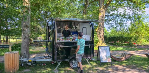 Ein Food-Truck bietet Snacks und Getränke an, während freundliche Interaktionen zwischen Verkäuferin und Kunde stattfinden.