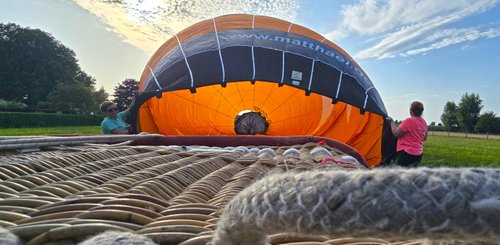 Hinter dem Korb, der gekippt auf dem Boden liegt, wird der orangefarbene Ballon mit heißer Luft gefüllt und bläst sich dadurch auf