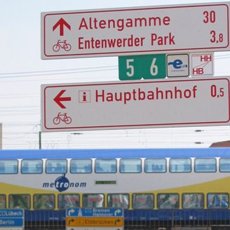 Beschilderung von Radwegen inklusive der Plakette zum Radfernweg Hamburg-Bremen vor einem metronom-Zug am Hamburger Hauptbahnhof