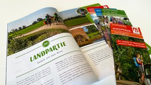 Mehrere Prospekte liegen auf einem Tisch, das Urlaubsmagazin ist aufgeklappt