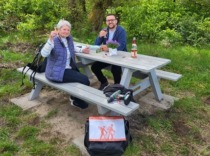 Florian Striebeck und Ingrid auf der neuen von ihr gespendeten Tisch-Bank-Kombination mit einem Glas alkoholfreien Sekt in der Hand