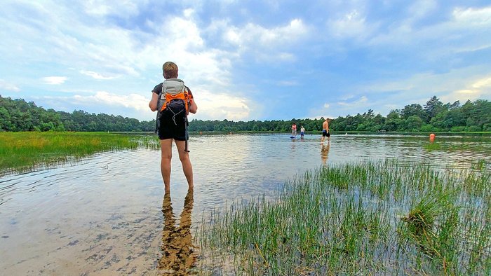 Frau mit Rucksack steht im seichten Wasser des Bullensees und schaut über den See