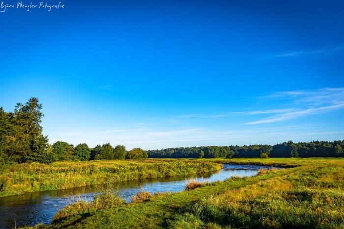 Der Fluss Wümme schlängelt sich durch die weite grüne Wümmeniederung unter tiefblauem Himmel