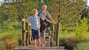 Eine Familie steht auf einer Brücke der Moorerlebniszone vom Tister Bauernmoor und schaut lachend in die Kamera