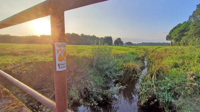 Brücke am Visselbach mit dem Schild vom ORTSWEG Buchholz bei Sonnenuntergang