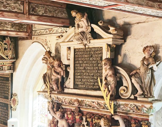 Epitaph mit fröhlich anmutenden Engeln und Weiner langen Textwidmung in goldener Schrift