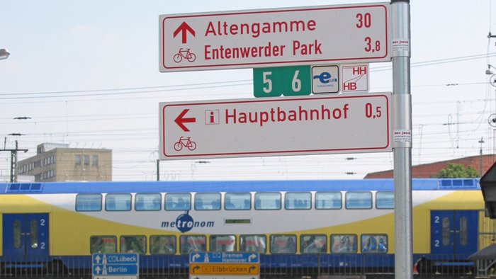 Beschilderung von Radwegen inklusive der Plakette zum Radfernweg Hamburg-Bremen vor einem metronom-Zug am Hamburger Hauptbahnhof