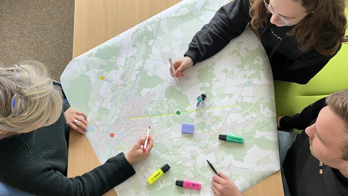 Drei Personen arbeiten mit bunten Stiften an einer Radkarte