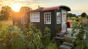 Ein alter Bauwagen, in dem übernachtet werden kann, vor einem Sonnenuntergang an einer Wiese