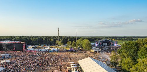 Ein riesiges Festivalgelände mit tausenden von begeisterten Menschen, die auf mehrere Bühnen blicken.