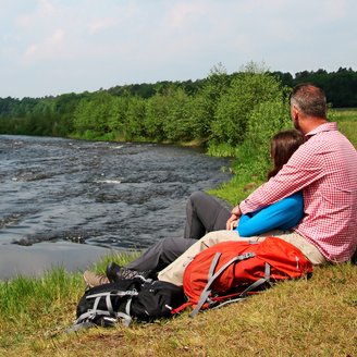 An einem Abschnitt der Wümme mit Stromschnelle kuschelt ein wanderndes Pärchen bei einer Pause