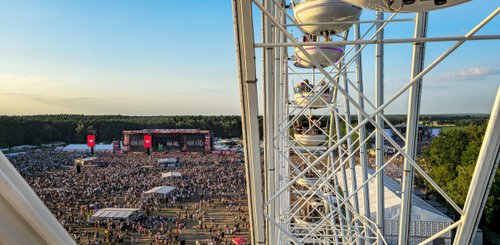 Blick von einem Riesenrad auf ein lebhaftes Festivalgelände, das von einer großen Menschenmenge besucht wird.