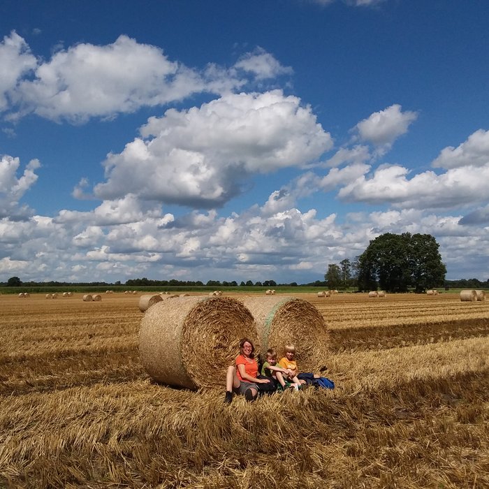 Eine Mutter sitzt auf einem Feld mit ihren beiden Söhnen vor zwei Strohballen