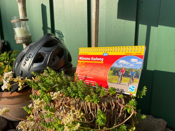 Ein schwarzer Fahrradhelm und die gedruckte Radkarte zum Wümme-Radweg sind in Blumentöpfen drapiert