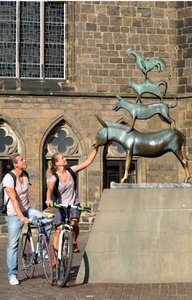 Zwei junge Radfahrer, vielleicht ein Paar, steht mit den Rädern an den Bremer Stadtmusikanten, sie berührt die Schnauze des Esels
