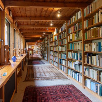 Langer gemütlicher Flur in Walter Kempowskis Haus mit Bücherregal auf der einen und Fensterfront zum Garten mit Figuren auf der anderen Seite