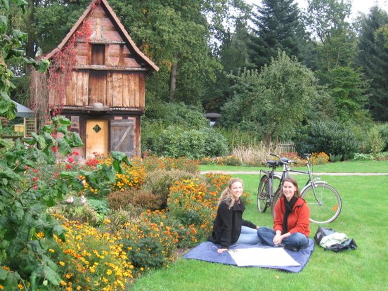 Zwei Radfahrerinnen machen eine Pause auf einer Picknickdecke mit der geöffneten Radkarte vor einem alten Fachwerkgebäude
