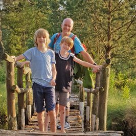 Eine Familie steht auf einer Brücke der Moorerlebniszone vom Tister Bauernmoor und schaut lachend in die Kamera