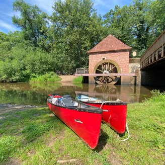 Zwei rote Kanus liegen am Ufer der Oste vor der historischen Wassermühle Eitzmühlen