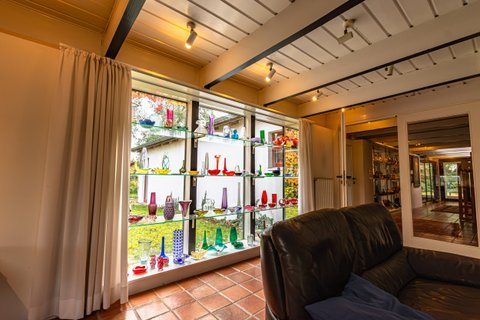 Glasvitrine mit bunten Vasen und Flaschen an einer Fensterfront im Haus Kreienhoop