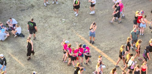 Eine Gruppe von Frauen in leuchtend pinken T-Shirts posiert fröhlich für ein Foto auf dem Festivalgelände.