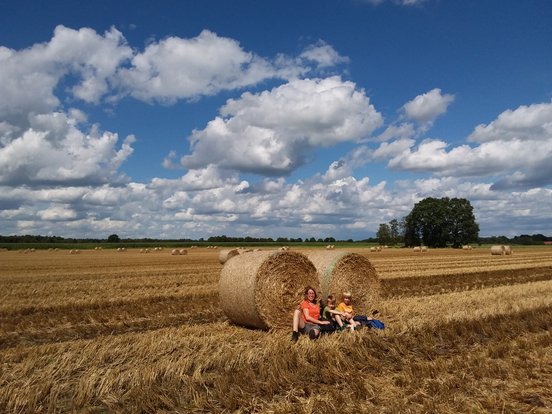 Eine Mutter sitzt auf einem Feld mit ihren beiden Söhnen vor zwei Strohballen