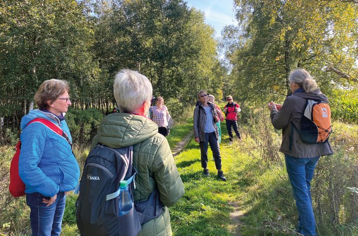 Eine Wandergruppe lauscht der Gästeführerin inmitten einer sattgrünen Natur