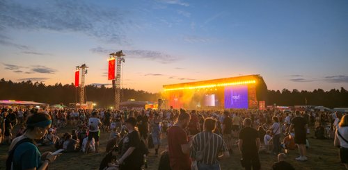 Eine lebhafte Menschenmenge versammelt sich vor einer aufwendig beleuchteten Bühne bei Sonnenuntergang.