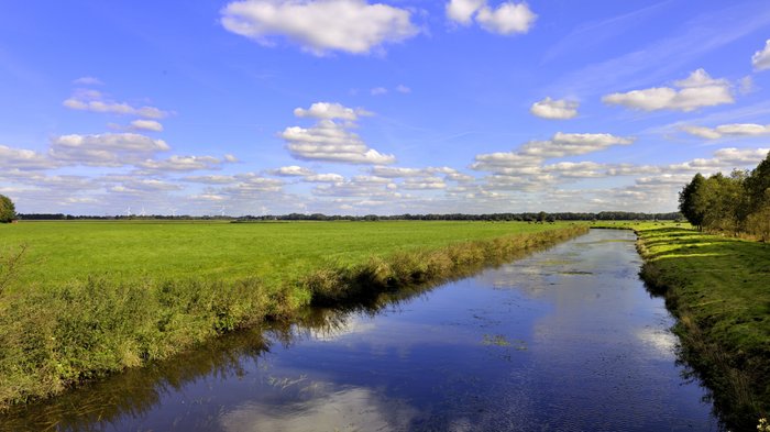 Kanal zwischen weiten und flachen Feldern, in dem sich der blaue Himmel spiegelt
