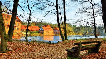 Die historische Ahauser Backsteinmühle hinter dem Mühlenteich in der Herbstsonne, davor eine Bank im Herbstlaub