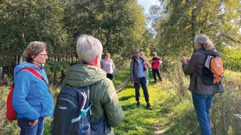 Eine Wandergruppe lauscht der Gästeführerin inmitten einer sattgrünen Natur