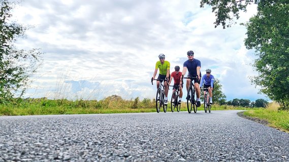 Blick von der Fahrbahn aus grauem Asphalt hinauf zu einer Gruppe Rennradfahrer