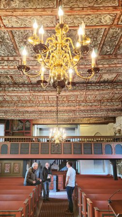 Blick auf den hinteren Bereich der Oeser Kirche mit Orgel, bemalter Decke und drei Personen im Gespräch