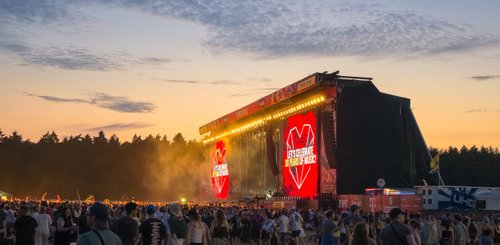 Die Bühne erstrahlt in hellem Licht mit einem großen Herzsymbol, während die Besucher im Sonnenuntergang das Festival genießen.