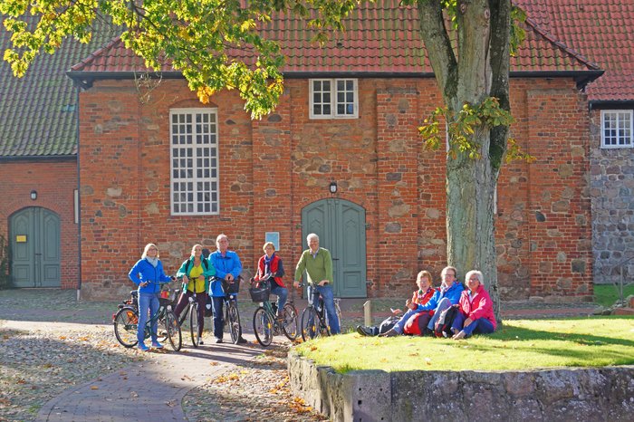 Eine Gruppe Radfahrer in bunter Kleidung macht eine Pause vor einer historischen Backsteinwand