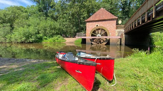 Zwei rote Kanus liegen am Ufer der Oste vor der historischen Wassermühle Eitzmühlen