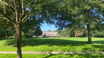 Hinter einer großen grünen Wiese ist das historische Fachwerk-Haus am See in Bremervörde klein zu sehen