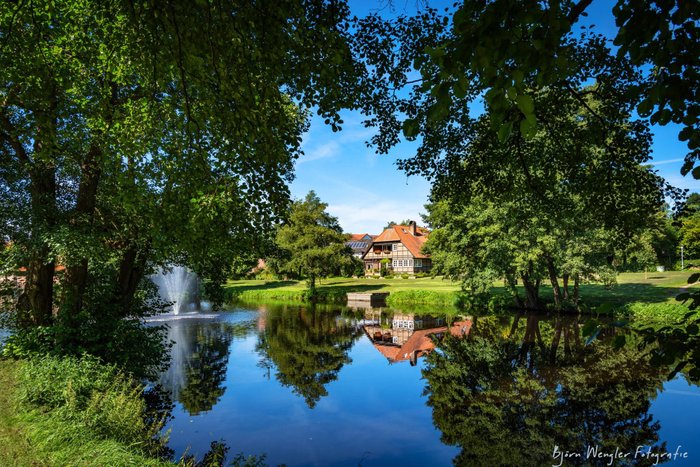 Der blaue Himmel spiegelt sich im Mühlenteich mit Springbrunnen in Sittensen, dahinter ist die Wassermühle zu sehen