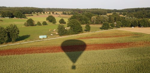 Der Schatten des Ballons fällt auf eine Landschaft mit rot-grünen leicht-welligen Feldern