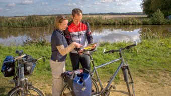 Zwei Radfahrer orientieren sich mit einer Karte in der Hand an der Wümme bei Ritterhude