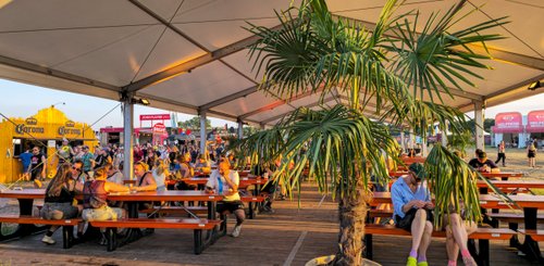 Schattige Tische unter einem Zelt laden Festivalbesucher ein, bei Essen und Trinken eine entspannte Zeit zu haben.