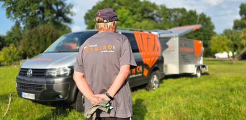 Ein Mitarbeiter von SkyMiro ist von hinten mit dem bedruckten Firmen-T-Shirt zu sehen, im Hintergrund das Auto mit dem Hänger