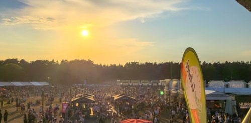 Die Sonne geht hinter einer lebhaften Festivalatmosphäre unter, wo Menschen in einer großen Menge fröhlich zusammen feiern.