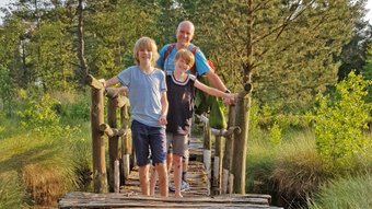 Eine Familie steht auf einer Brücke der Moorerlebniszone vom Tister Bauernmoor und schaut lachend in die Kamera