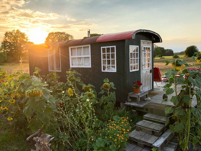 Ein alter Bauwagen, in dem übernachtet werden kann, vor einem Sonnenuntergang an einer Wiese